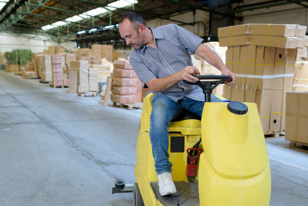 man cleaning warehouse using ride-on machine